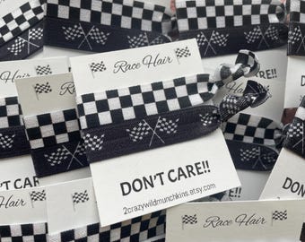 Op de afbeelding: Een collectie elastische haarelastiekjes met een zwart-wit geblokt patroon en een kleine afbeelding van gekruiste finishvlaggen. Elk haarelastiekje zit op een witte kaart met de tekst Race Hair en DON'T CARE!!