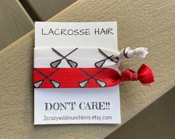 May include: Two red and white elastic hair ties with a lacrosse stick design. The hair ties are on a white card with the text "Lacrosse Hair Don't Care!! 2crazywildmunchkins.etsy.com"