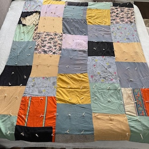 May include: A patchwork quilt composed of various fabric squares in a range of colors including black, yellow, orange, and gray. Some squares feature tropical print patterns. The quilt is handmade and laid out on a white bed.