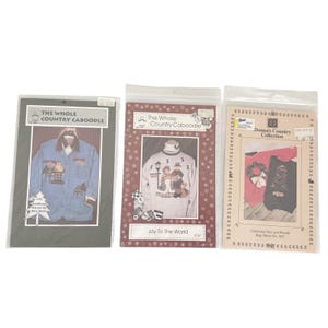 May include: Three sewing patterns in plastic sleeves. The left shows a blue jacket with a Santa graphic. The center shows a white sweatshirt with a holiday scene and the text Joy To The World. The right shows a red and black shirt with tree and wreath graphics.