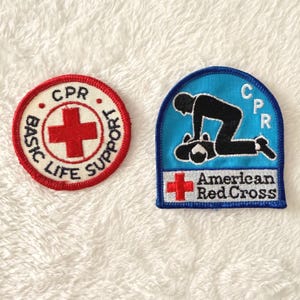 May include: Two embroidered patches. One is round with a red cross and the words "BASIC LIFE SUPPORT" and "CPR". The other is a blue arch shape with a CPR graphic and "American Red Cross" text.
