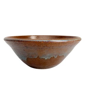 May include: A wide, round ceramic bowl with a smooth, glossy finish. The exterior features a deep, earthy brown glaze that transitions into a subtle, muted blue-grey tone near the base and rim, creating a distinct, layered color effect.