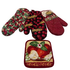 May include: A set of three oven mitts and one square pot holder. The mitts feature apple patterns in red, green, and black with text reading APPLES. The pot holder displays a central illustration of whole and sliced red apples with green leaves.