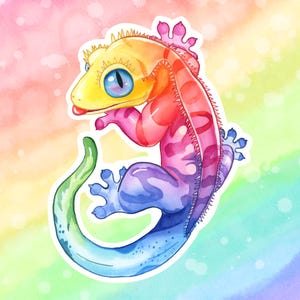 Peut inclure: Illustration aquarelle d'un gecko aux couleurs de l'arc-en-ciel. Le gecko est représenté avec des couleurs vives : jaune, orange, rouge, rose, violet, bleu et vert. Il a de grands yeux bleus sur un fond aux couleurs de l'arc-en-ciel.