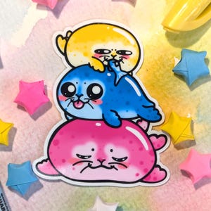 May include: A stack of three cartoon sea animal stickers. The bottom sticker is pink and has a grumpy expression. The middle sticker is blue and has a friendly expression. The top sticker is yellow and has a surprised expression.