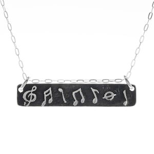 May include: A silver necklace with a black rectangular pendant featuring a treble clef and musical notes.
