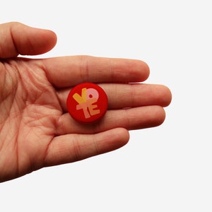 May include: A red round button with the word "VOTE" written in yellow, orange, and pink letters.
