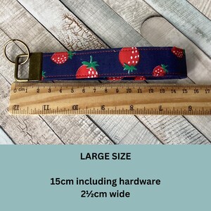 May include: A navy blue key fob with a repeating pattern of red strawberries with green leaves. The key fob is 15cm long including hardware and 2.5cm wide. The text "LARGE SIZE" is visible.