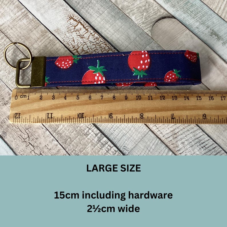 May include: A navy blue key fob with a repeating pattern of red strawberries with green leaves. The key fob is 15cm long including hardware and 2.5cm wide. The text "LARGE SIZE" is visible.