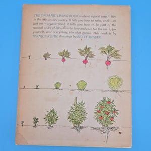 May include: The back cover of a vintage book titled "The Organic Living Book." The cover features illustrations of various plants with roots, including radishes, cabbages, and tomato plants. Text on the cover describes the book's focus on organic living.