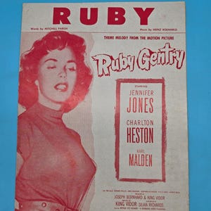 May include: Sheet music cover for "Ruby" featuring a red-toned image of a woman and the title in large red letters. The cover includes the names of the stars Jennifer Jones, Charlton Heston, and Karl Malden. The music is by Heinz Roemheld.