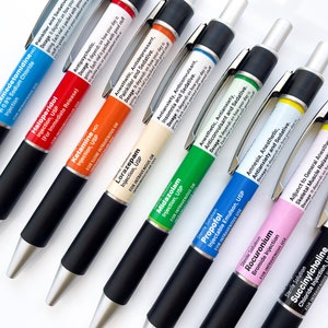 May include: A collection of black pens with silver tips and black grips. Each pen has a colored label with white text, listing various medications such as Dexmedetomidine, Haloperidol, and Ketamine. The pens are arranged diagonally on a white surface.