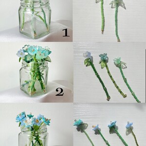 May include: Three sets of handcrafted flower-shaped charms with green beaded stems. Set 1 features two blue flowers, set 2 has three light blue and green flowers, and set 3 includes four blue and white flowers. Each set is displayed in a glass jar.