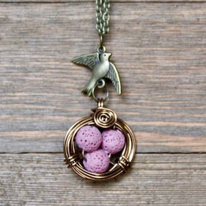 Puede incluir: Un collar de oro con un dije de pájaro y un nido de alambre con huevos de roca de lava rosa.