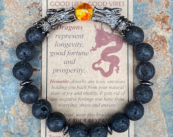 May include: Black lava rock beaded bracelet with silver dragon head charms and an orange and yellow glass bead. The bracelet is accompanied by a card that reads "Good Life Good Vibes" and describes the meaning of the bracelet.