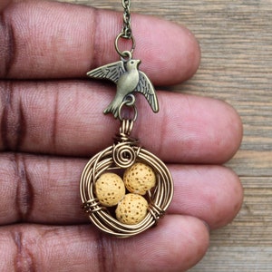 Puede incluir: Un collar de oro con un dije de pájaro y un nido envuelto en alambre con tres huevos de roca de lava amarilla.