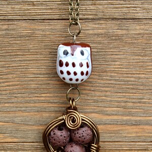 Puede incluir: Un dije de b&uacute;ho marr&oacute;n y blanco cuelga de una cadena dorada. El dije de b&uacute;ho est&aacute; unido a una jaula de alambre con cuatro cuentas de roca de lava marr&oacute;n en su interior.