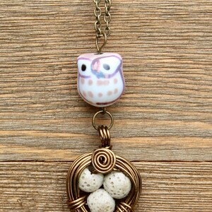 May include: A gold necklace with a ceramic owl pendant and a wire-wrapped nest with white lava rock beads.