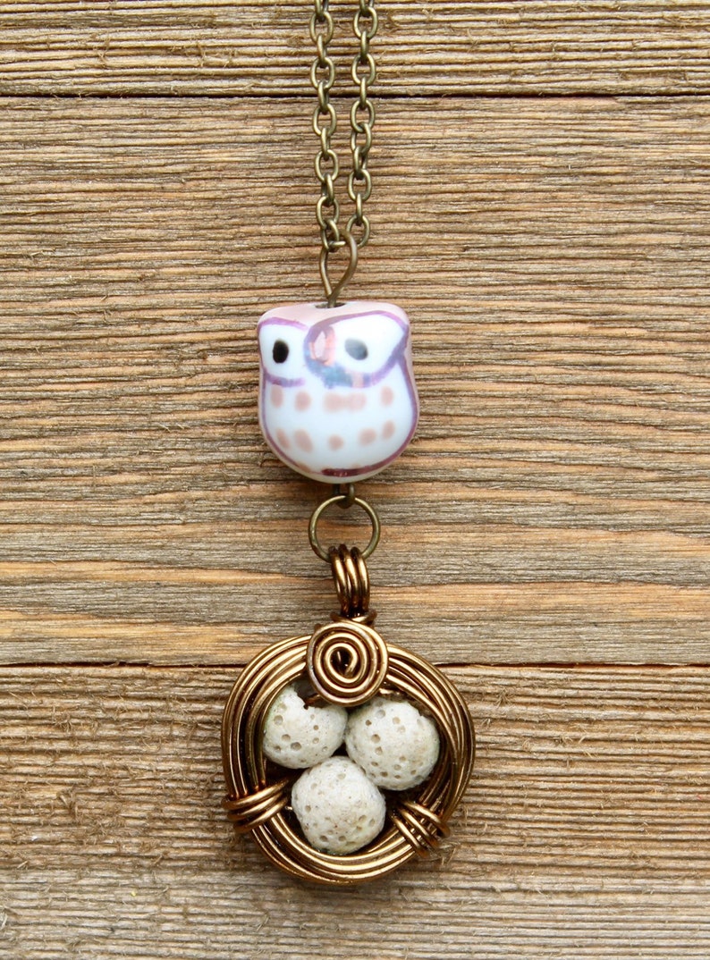 May include: A gold necklace with a ceramic owl pendant and a wire-wrapped nest with white lava rock beads.