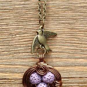 May include: A copper wire necklace with a bird charm and a lavender lava rock nest pendant.