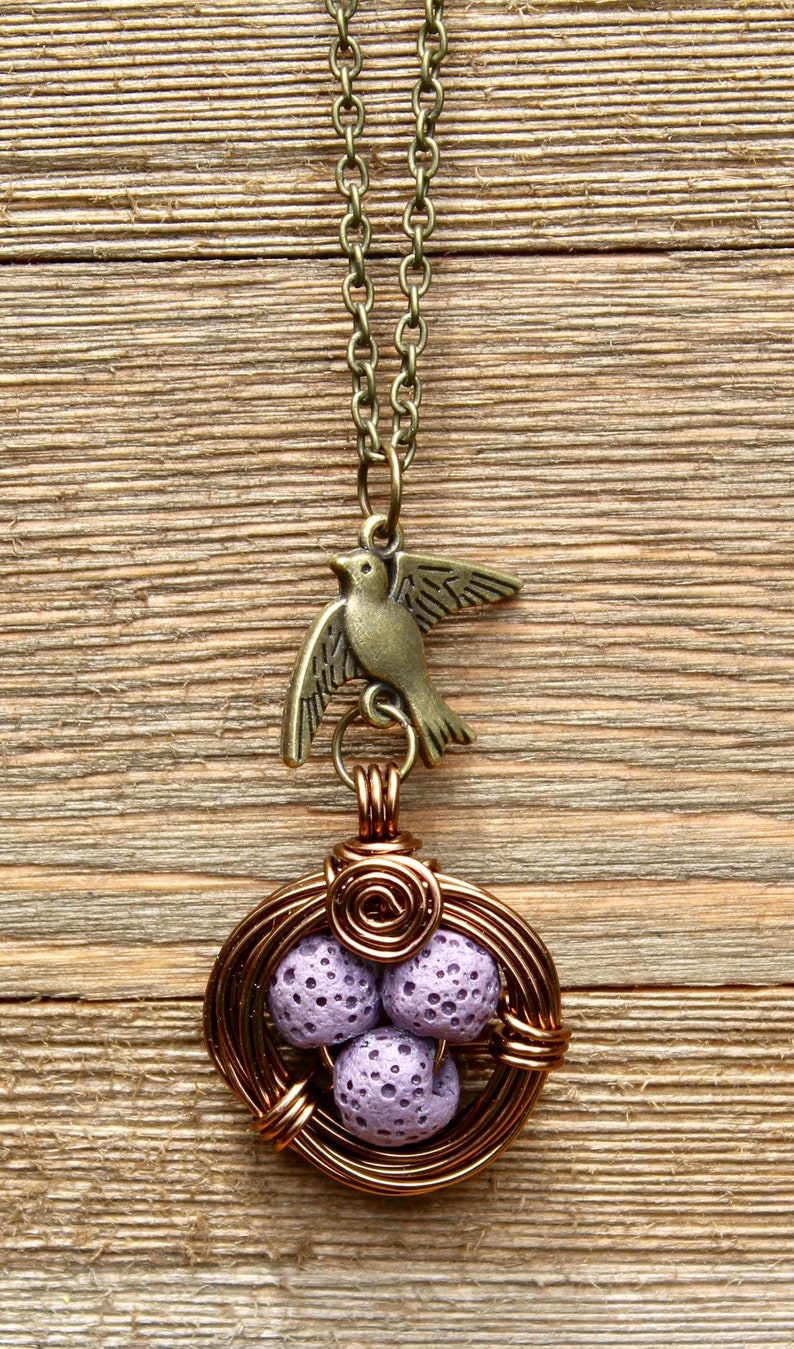 May include: A copper wire necklace with a bird charm and a lavender lava rock nest pendant.