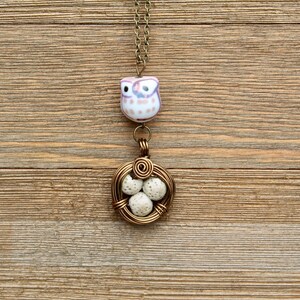 May include: A gold wire necklace with a ceramic owl charm and a wire nest with white eggs.