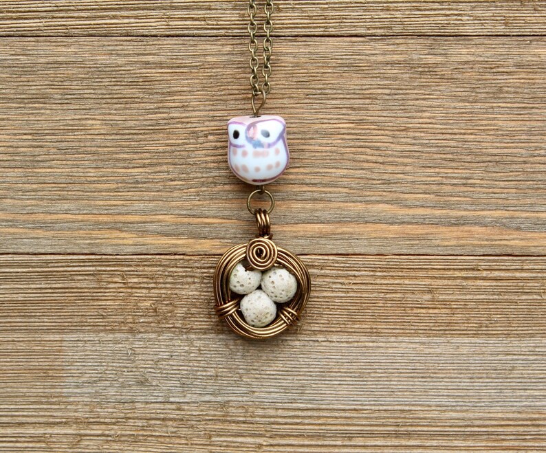 May include: A gold wire necklace with a ceramic owl charm and a wire nest with white eggs.