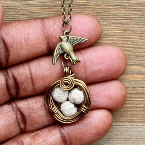 Puede incluir: Un collar de oro con un dije de pájaro y un nido envuelto en alambre con huevos blancos.