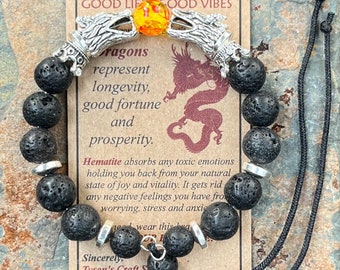 May include: Black lava rock beaded bracelet with silver dragon head charms and a hematite bead. The bracelet is on a card that reads "Good Life Good Vibes" and includes a description of the meaning of the bracelet.