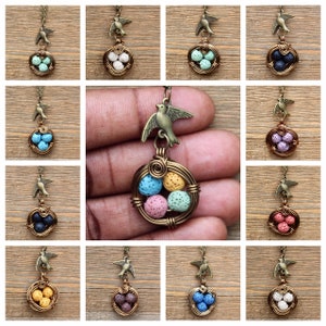 May include: A necklace with a bird charm and a wire nest with five lava rock eggs in various colors. The colors of the eggs are pink, blue, yellow, green, and white.