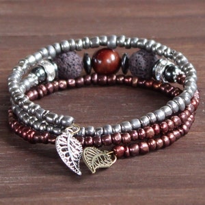 May include: A multi-strand bracelet with silver and burgundy beads, lava rock beads, a red gemstone, and two silver leaf charms.
