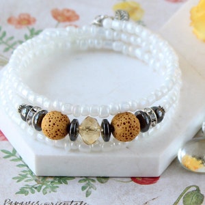 May include: White beaded wrap bracelet with brown lava rock beads, a clear crystal bead, and silver accents.