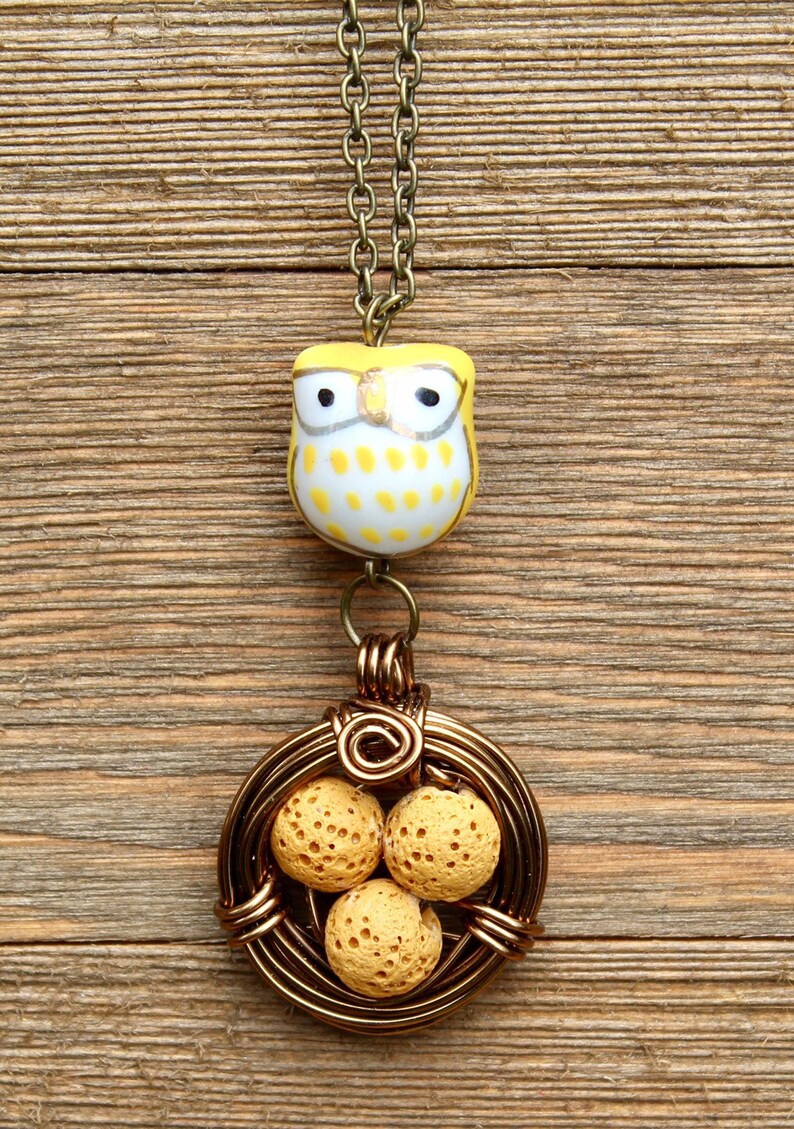 K&ouml;nnte beinhalten: Eine Halskette mit einem gelben Eulenschmuckst&uuml;ck und einem drahtgewickelten Nestanh&auml;nger mit drei gelben Lavasteinen.