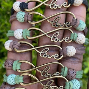 May include: Six infinity symbol bracelets with the word "love" inscribed on each. The bracelets are made with brown leather cord, green and white lava beads, and gold-toned metal infinity symbols.