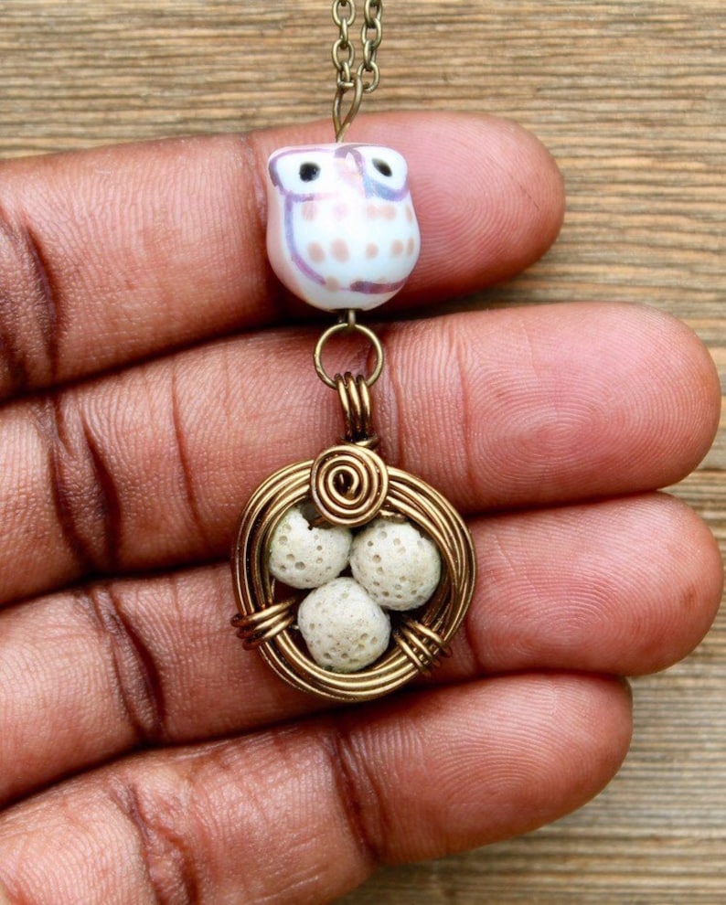 May include: A gold wire nest pendant necklace with three white lava rock eggs and a pink and white owl bead.