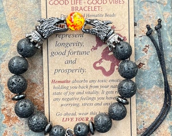 May include: Black lava rock beaded bracelet with silver dragon head charms and a single orange gemstone. The bracelet is accompanied by a card that reads "Good Life - Good Vibes Bracelet: Dragon Head Hematite Beads represent longevity, good fortune and prosperity. Hematite absorbs any toxic emotions holding you back from your natural state of joy and vitality. It gets rid of any negative feelings you have worrying, stress and anxiety. Go ahead, wear this bracelet. LIVE YOUR BEST LIFE."