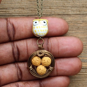 Puede incluir: Un collar de oro con un dije de búho amarillo y un nido envuelto en alambre con tres cuentas amarillas.