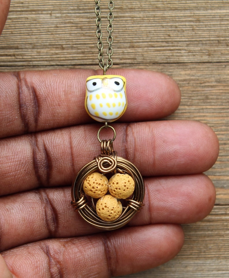 K&ouml;nnte beinhalten: Eine goldene Halskette mit einem gelben Eulenschmuckst&uuml;ck und einem drahtgewickelten Nest mit drei gelben Perlen.