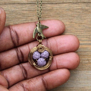 May include: A gold wire bird nest pendant necklace with a purple lava rock egg charm and a bronze bird charm.