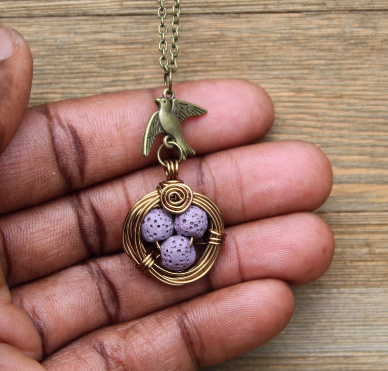 May include: A gold wire bird nest pendant necklace with a purple lava rock egg charm and a bronze bird charm.
