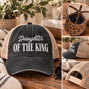 May include: A black distressed baseball cap with a tan mesh back and an adjustable snapback closure. The front features the white text Daughter OF THE KING. The interior of the cap displays a brown and black leopard print pattern on the fabric.