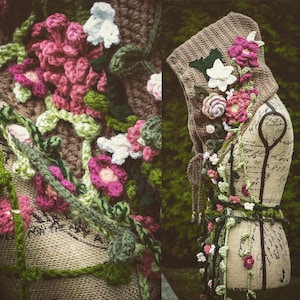 May include: A crocheted hooded scarf with floral embellishments in shades of pink, white, and green. The scarf is draped over a mannequin with a handwritten note on the torso.