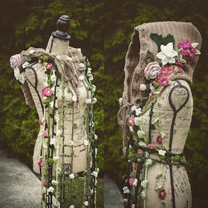 May include: Two crocheted hooded garments with floral embellishments. The garments are displayed on mannequins with a vintage floral pattern. The garments are made with a variety of colors, including green, brown, white, and pink.