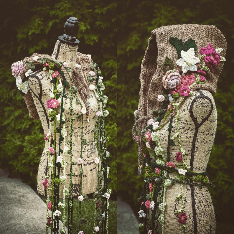 May include: Two crocheted hooded garments with floral embellishments. The garments are displayed on mannequins with a vintage floral pattern. The garments are made with a variety of colors, including green, brown, white, and pink.