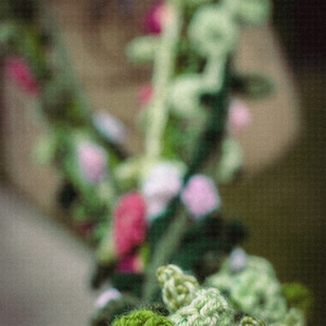 May include: A close-up of a crocheted garland with green leaves and pink flowers. The garland is made of yarn and is a handmade craft.