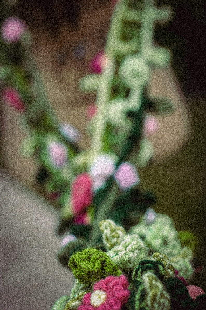 May include: A close-up of a crocheted garland with green leaves and pink flowers. The garland is made of yarn and is a handmade craft.
