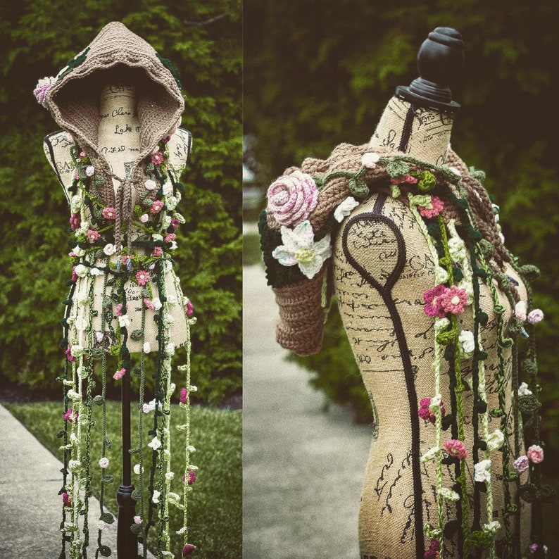May include: A crocheted hooded top and matching shawl with floral and vine details. The top has a brown hood and the shawl has a brown base with green vines and pink flowers.