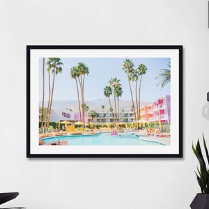 K&ouml;nnte beinhalten: Ein gerahmtes Foto eines modernen Motels aus der Mitte des Jahrhunderts mit einem Swimmingpool im Vordergrund. Das Motel ist in den Farben Rosa, Gelb und Wei&szlig; gestrichen. Palmen s&auml;umen den Pool und die Umgebung. Das Foto ist aus leicht erh&ouml;hter Perspektive aufgenommen und bietet einen guten Blick auf den Pool und das Motel.