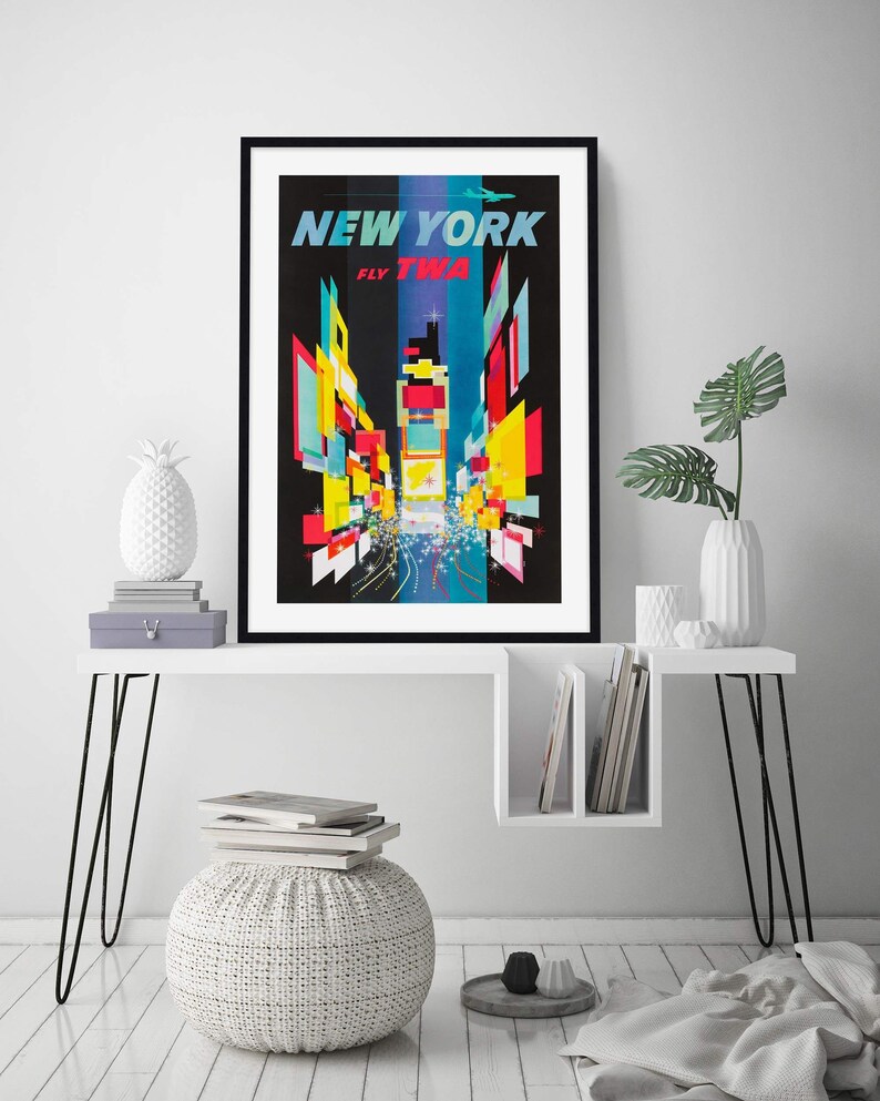 Pu&ograve; includere: Un poster vintage di viaggio che pubblicizza un viaggio a New York City con il testo "New York Fly TWA". Il poster presenta una rappresentazione astratta e colorata di Times Square di notte.