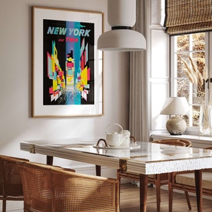 Pu&ograve; includere: Una sala da pranzo con un tavolo bianco con piano in marmo e una lampada a sospensione in ceramica bianca sopra di esso. Ci sono quattro sedie in vimini intorno al tavolo e un poster vintage di New York City sulla parete dietro il tavolo.